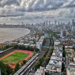A sweeping view of Marine Drive, with the railway tracks, a sports ground, and the city's dense residential buildings all in one frame. This image captures the multi-layered life of Mumbai along its famous coastline.