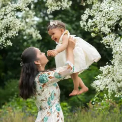 A mother lifts her daughter up high amidst blooming white flowers. This outdoor family photoshoot captures a moment of pure joy and connection.