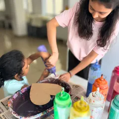 Teamwork makes the dream work. A younger child gets a helping hand from an older sister or mentor to pour the paint, making it a great bonding activity.