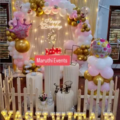 A beautiful birthday setup for Yashwita, featuring a pink and gold balloon arch, elegant white plinths, and a charming picket fence accent.