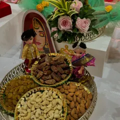A healthy and beautiful dry fruit platter. This arrangement includes cashews, almonds, raisins, and dates, decorated with couple dolls for an engagement ceremony.