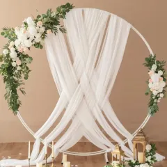 An elegant and minimalist ring ceremony backdrop. This design uses a clean white circular frame, gracefully draped with sheer white fabric and accented with asymmetrical arrangements of white roses and lush green eucalyptus for a sophisticated and modern feel.