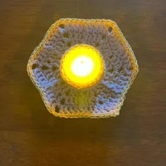 A top-down view of the hexagonal tealight holder, showing the intricate crochet pattern. The golden yarn border adds an extra festive sparkle when it catches the light.