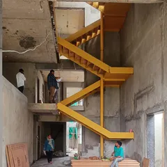 A vibrant yellow metal staircase is installed during the construction of the Jayanagar Residence. This image captures a key moment in the building process, showing how a bold design element begins to define the character of the interior space.