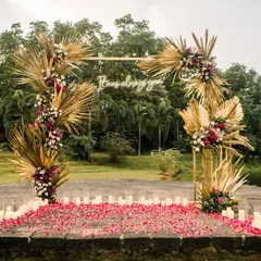 A daytime view of the proposal stage, set against a serene lake. The boho arch with golden palms and deep florals stands out beautifully.