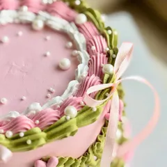 A close-up on the detailed piping work, showing the layers of pink, white, and green buttercream, the scattered pearls, and the soft texture of the satin ribbon.