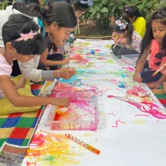 A group of children completely absorbed in a collaborative painting session at one of our outdoor art picnics. Working together on a single large canvas fosters teamwork and shared creativity.