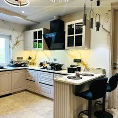 The stunning 'after' shot of a kitchen renovation in Amar Colony. I used a classic white and black theme with a marble backsplash, modern appliances, and a functional breakfast counter to completely transform the space.