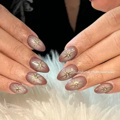 A beautiful example of aura nails. This set features a soft brown aura effect with a gold starburst charm in the center of each nail.