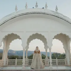 A breathtaking wide shot of the bride standing in a white marble pavilion at Nahargarh Palace, with the Aravalli hills providing a stunning backdrop.
