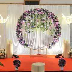 A breathtaking engagement or reception stage with a cascading purple floral ring, large flower-shaped lamps, and dramatic lighting.