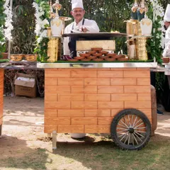 A chef stands ready at a beautifully decorated wooden thela cart. The cart is equipped with elegant serving dishes, ready to provide guests with a unique and interactive food experience.