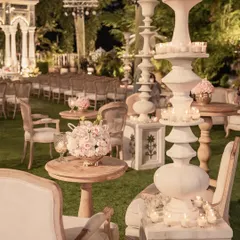 Candlelit ambiance for an evening garden wedding. Sculptural candle stands and soft floral arrangements create intimate seating nooks for guests, set against the backdrop of a grand, illuminated mandap.