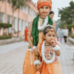 A full-length portrait of two children dressed as the divine couple Radha and Krishna. This photo captures their innocent expressions and traditional attire against the backdrop of Hanuman Dham in Jim Corbett.