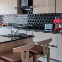 This open kitchen, with its beautiful breakfast table, is the heart of this Mumbai home. I designed it to be perfect for creating memories, with black triangular tiles, warm wood, and a pop of red from the coffee machine.