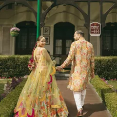 Walking hand-in-hand, this couple's coordinated Haldi outfits are a perfect match. Her colorful lehenga and his printed kurta create a cohesive and stylish look.