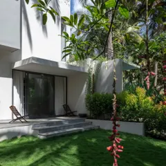 A quiet sit-out area on the east side of the house, perfect for enjoying the morning sun. The simple steps and patio create a gentle transition from the interior living space to the manicured lawn.