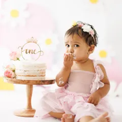 A tentative first taste. This little birthday girl is curiously sampling the frosting, and her expression is absolutely priceless. The daisy-themed background adds a sweet, cheerful touch.
