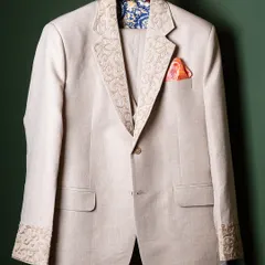 Craftsmanship is visible in the details. This bespoke linen jacket features intricate, hand-guided embroidery on the lapels and cuffs, paired with a vibrant silk pocket square. It is a testament to our dedication to creating garments that are unique and timeless.