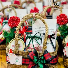 A festive Christmas hamper in a rustic woven basket. It's packed with holiday goodies and adorned with a plaid ribbon, a Santa tag, and other Christmas-themed decorations.
