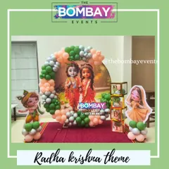 A complete Radha Krishna theme baby shower setup. This includes a circular backdrop with a divine print, themed cutouts of little Radha and Krishna, and balloon blocks spelling 'BABY'.