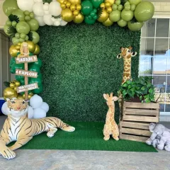 For this safari-themed party, I used a green hedge backdrop, a balloon arch in shades of green and gold, and large plush animals like a tiger and giraffe to create an exciting atmosphere.
