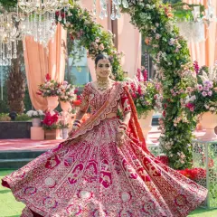 A classic bridal twirl showcasing the magnificent red lehenga against a backdrop of lush floral arches. This portrait captures the grace and happiness of the bride on her special day.