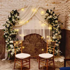 A simple and elegant setup for an intimate ring ceremony or home engagement. We used a circular arch decorated with white flowers and sheer drapes, illuminated by fairy lights to create a warm and romantic photo corner.