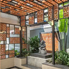 A tranquil outdoor alcove designed for a Ganesha statue. The space uses a combination of terracotta jali screens, laterite stone, and lush greenery to create a modern yet sacred-feeling shrine.