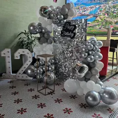 A chic and modern 12th birthday party setup in silver and white. This includes a silver sequin backdrop, a balloon garland, and large marquee numbers for the age.