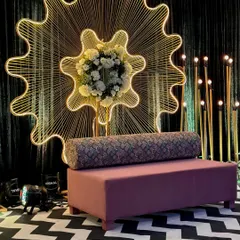 A modern and chic stage backdrop for a cocktail party, featuring a large, illuminated gear-shaped structure. The black-and-white chevron flooring and minimalist sofa complete this unique and stylish look.