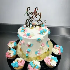 A "Baby in Bloom" celebration set featuring a main cake and matching cupcakes. The delicate floral piping in pink, blue, and white creates a beautiful garden theme for the special day.