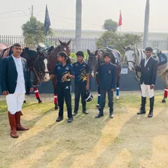 Our team of riders and instructors, dressed in formal competition attire, stand with their equine partners during a sports event.