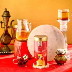 A vibrant and regal composition for Hindraj's Tangerine Thakur Tea. The bold red and gold background complements the packaging and creates a feeling of luxury and warmth.