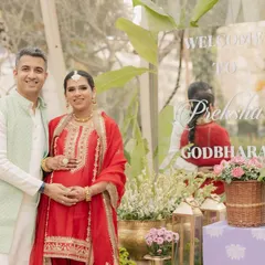 The happy couple at the entrance of their Godh Bharai ceremony, featuring a custom acrylic welcome sign.