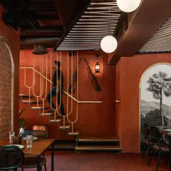 The sleek, minimalist staircase at 'Chambal' is a design feature in itself. Its delicate metalwork contrasts with the earthy red walls and rustic artifacts, creating a point of visual interest.