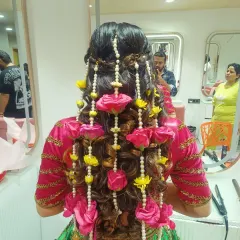 For a vibrant Mehendi function, I created this playful and intricate hairstyle featuring cascading curls and braids. The style is heavily adorned with strings of pearls and bright pink and yellow fresh flowers.