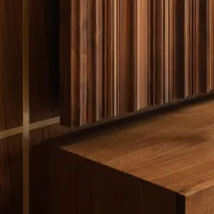 The rhythmic pattern of fluted walnut paneling creates a beautiful play of light and shadow. This detail shot highlights the precise craftsmanship required to achieve such a seamless and textured surface, enhanced by a subtle brass inlay.