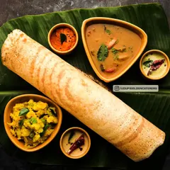 A classic South Indian Masala Dosa, served on a traditional banana leaf with fresh coconut chutney, spicy red chutney, and flavorful sambar. This is a highlight of our live dosa counters and breakfast menus.