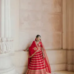 A regal portrait of Nikki in her red Sabyasachi lehenga. The architectural details of the palace provide a grand and fitting backdrop.