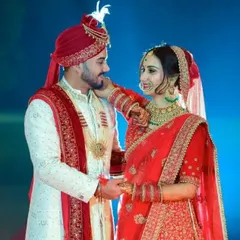 This classic red and white combination is a favorite for wedding ceremonies. The bride is in a bright red lehenga with gold work, and the groom wears an elegant white sherwani with red and gold accents on the collar and stole.