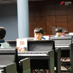 The beginning of a performance journey. Young students at their keyboards look out at the audience during their annual school recital, a foundational experience in building stage presence.