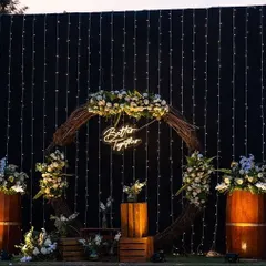 A rustic yet glamorous pre-wedding photo corner with a 'Better Together' neon sign, a wooden wreath, and a backdrop of fairy lights.