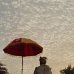 An artistic shot of the groom under a traditional umbrella against a dramatic, cloud-filled sky. This image captures a sense of grandeur and cultural richness.