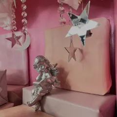 A close-up look at one of the silver angel figurines, sitting amongst soft pink gift boxes and sparkling star and moon decorations. These little details are what make a baby gift truly heavenly.