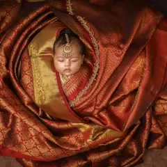 This stunning portrait captures a newborn wrapped in the rich fabric of a traditional red and gold saree. The intricate details of the fabric create a luxurious and culturally rich setting for this peaceful moment.