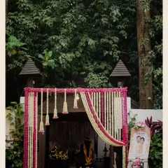 The beautifully decorated entrance to a wedding ceremony. The traditional floral hangings and a welcome sign with the couple's caricature set a warm and inviting tone for the guests.