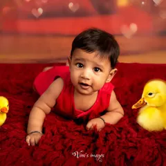 Tummy time with some feathered friends. This cute infant portrait captures a baby's curiosity as he lies on a bright red rug with two little ducklings.