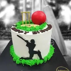 A black forest cricket cake for a true fan. The design features a batsman silhouette, a vibrant red cricket ball, and wickets on a grassy green top.