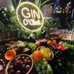 It's always Gin O'Clock at my speakeasy-style gin bar. This setup features a lush display of fresh fruits and botanicals, premium gins like Hendrick's, and a cool neon sign to complete the vibe.
